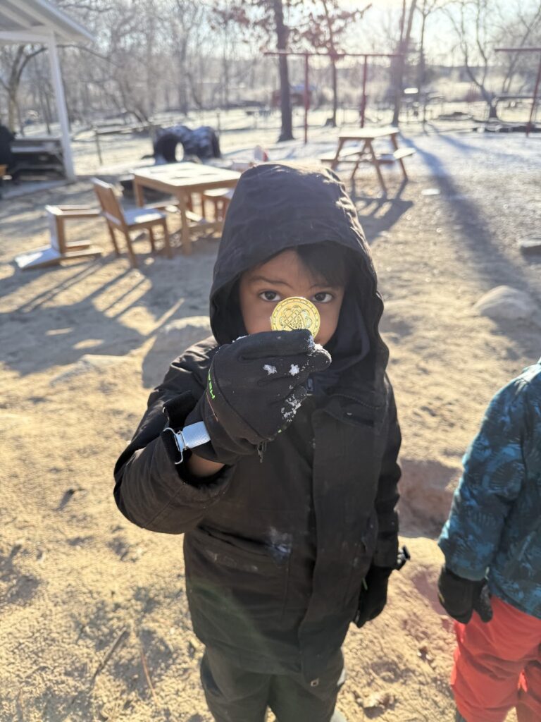 Preschool child proudly holding a gold coin found during St. Patrick's Day nature walk and treasure hunt at Farm School